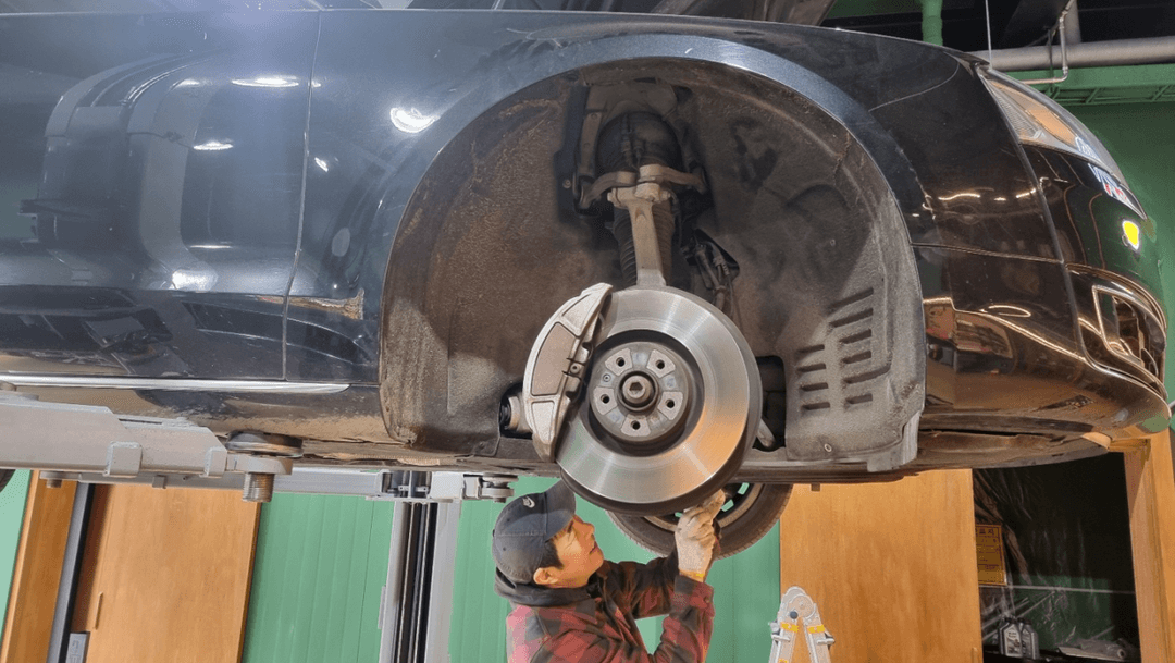 정비사가 리프트 위 수입차 브레이크를 점검하는 모습